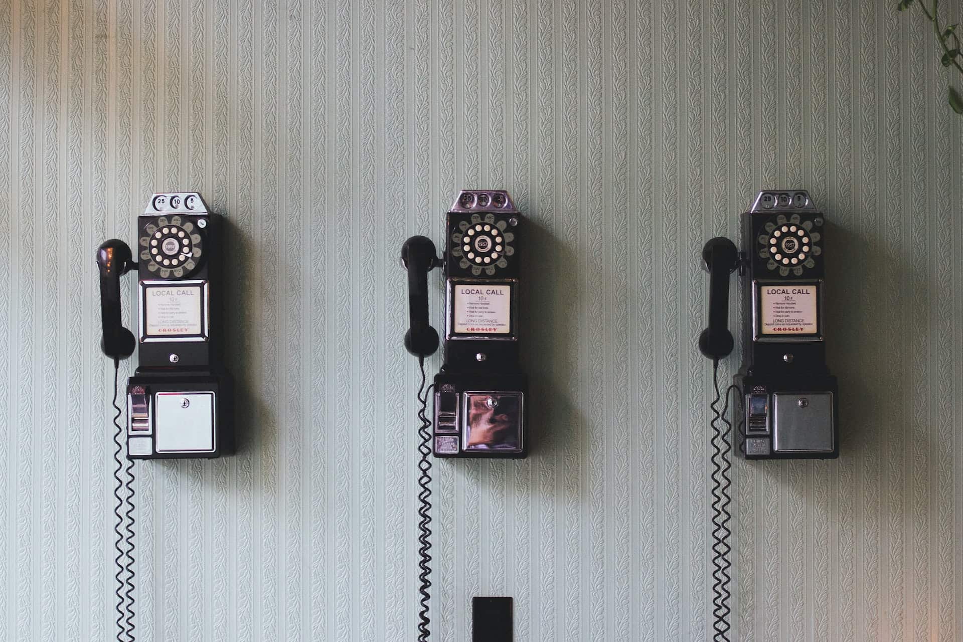 Alt tag: "Three vintage black rotary dial telephones mounted on a wall with elegant wallpaper, symbolizing direct communication, for the blog post '5 Essentials to Include on Your Contact Page' by Wild Wattle Digital